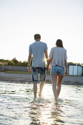 Rückansicht eines jungen Paares, das sich an den Händen hält und im Wasser am Strand spazieren geht - MASF06001