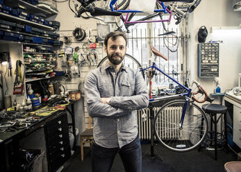 Portrait of mid adult male owner standing arms crossed at bicycle repair shop - MASF06042