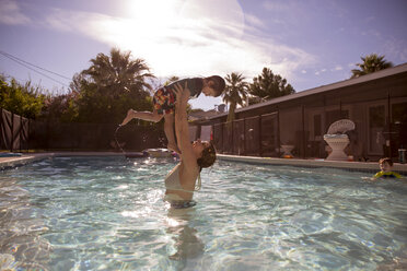 Glückliche Mutter, die einen Jungen im Schwimmbad eines Ferienortes hochhebt - CAVF44097