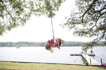 Girl enjoying on tire swing at lakeshore - CAVF44101