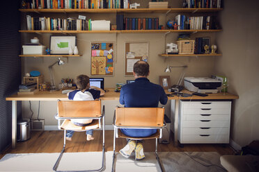 Rear view of father and son using laptop computer at home - CAVF44114