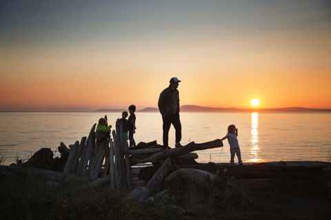 Vater mit Kindern am Strand bei Sonnenuntergang, lizenzfreies Stockfoto