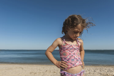 Nettes Mädchen steht mit Händen auf der Hüfte am Strand gegen den Himmel - CAVF44156