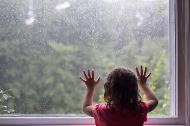 Rückansicht eines Mädchens, das durch ein Glasfenster den Schneefall betrachtet - CAVF44158
