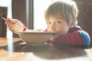 Porträt eines Jungen, der sich zu Hause an den Tisch lehnt und isst - CAVF44181