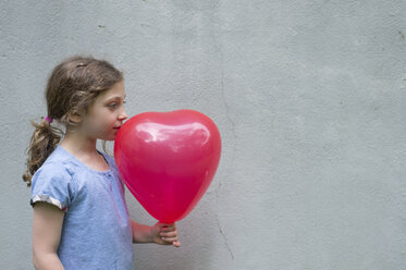 Side view of girl looking away while holding balloon against wall - CAVF44190