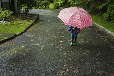 Niedriger Ausschnitt eines Mädchens, das mit einem Regenschirm auf einen Fußweg springt, lizenzfreies Stockfoto