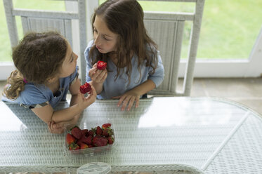 Hohe Winkel Ansicht der Schwestern Blick auf Gesicht zu Gesicht beim Essen Erdbeeren am Tisch - CAVF44194
