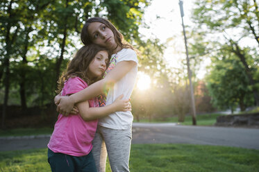 Schwestern umarmen sich im Park stehend - CAVF44205