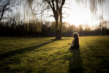 Girl sitting on grassy field during sunset - CAVF44233