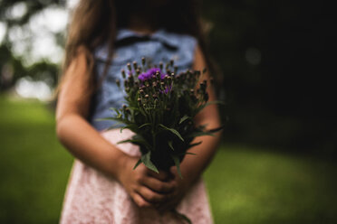 Midsection of girl holding leaves and flowers while standing in forest - CAVF44236