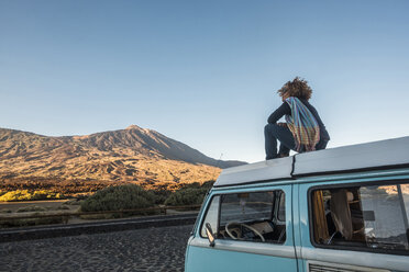 Carefree woman sitting on camper trailer against mountains and clear sky - CAVF44241