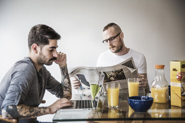 Schwuler Mann benutzt Laptop, während sein Partner am Frühstückstisch Zeitung liest - CAVF44277