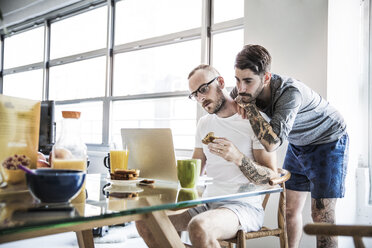 Homosexuelles Paar schaut beim Frühstück am Tisch in den Laptop - CAVF44281