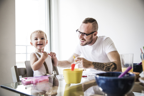 Glücklicher Vater füttert Tochter am Frühstückstisch an der Wand, lizenzfreies Stockfoto