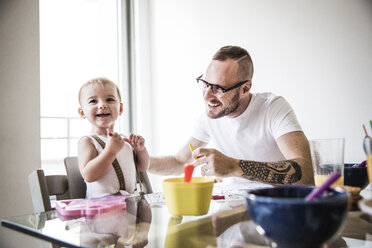 Glücklicher Vater füttert Tochter am Frühstückstisch an der Wand - CAVF44287
