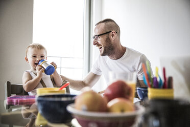 Glücklicher Vater sieht seine Tochter beim Trinken im Wohnzimmer an - CAVF44294