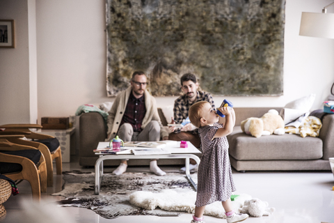 Väter sehen ihre Tochter beim Trinken an, während sie im Wohnzimmer stehen, lizenzfreies Stockfoto