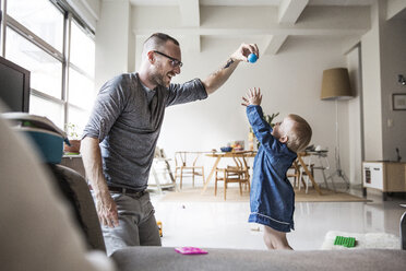 Happy father playing with daughter in living room at home - CAVF44310