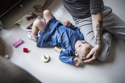 Hoher Blickwinkel des Vaters, der neben seiner Tochter sitzt, die zu Hause auf dem Boden liegt, lizenzfreies Stockfoto