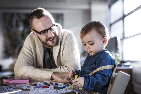 Lächelnder Vater, der mit seiner Tochter am Tisch malt, lizenzfreies Stockfoto