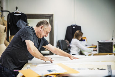 Fashion designer working at table with coworker sitting in background - CAVF44333