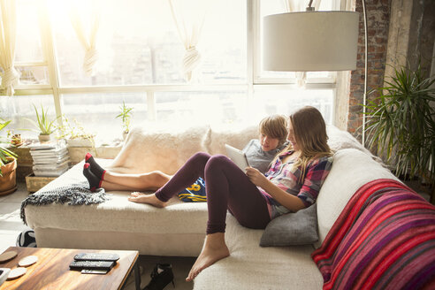 Kinder schauen auf einen Tablet-Computer, während sie auf dem Sofa im Wohnzimmer sitzen - CAVF44391