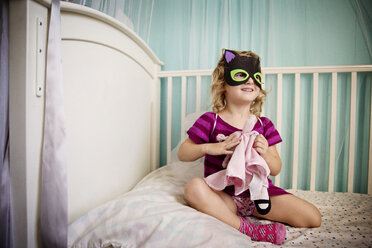 Niedliches Mädchen mit Maske, das mit einer Puppe spielt, während es in einem Kinderbett sitzt - CAVF44411