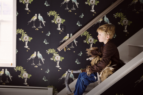 Seitenansicht eines Jungen, der ein Kostüm hält, während er zu Hause auf einer Treppe sitzt, lizenzfreies Stockfoto