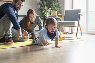 Happy parents looking at son crawling on floor at home - CAVF44459