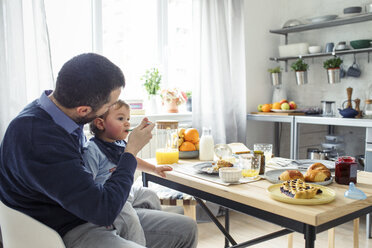 Vater gibt seinem Sohn am Küchentisch Frühstück - CAVF44465