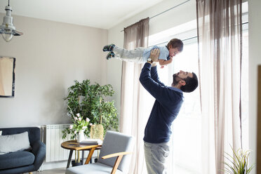 Playful man carrying son while standing by window at home - CAVF44470