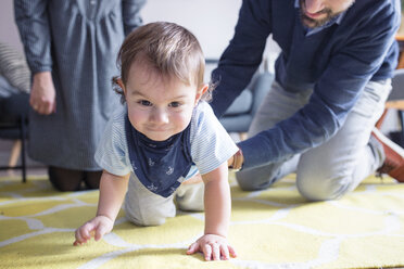 Happy parents looking at son crawling on carpet at home - CAVF44473