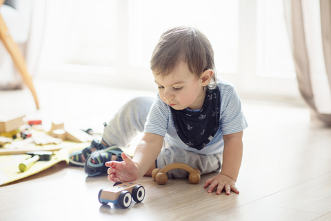 Kleiner Junge spielt mit Spielzeug, während er zu Hause auf dem Boden sitzt, lizenzfreies Stockfoto