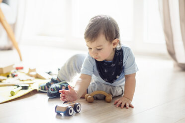 Baby boy playing with toys while sitting on floor at home - CAVF44476