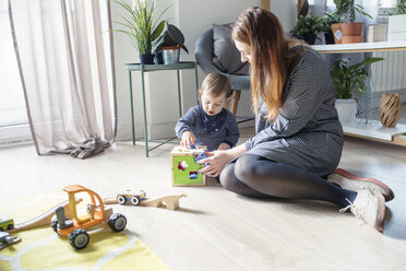 Mutter und Sohn spielen mit Spielzeug, während sie zu Hause auf dem Boden sitzen - CAVF44478