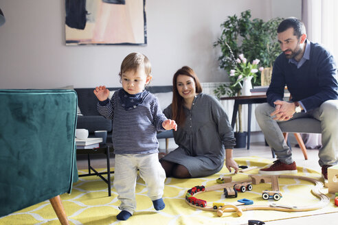 Glückliche Eltern sehen ihren Sohn im Wohnzimmer laufen - CAVF44481