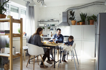Eltern betrachten ihren Sohn, der auf einem Hochstuhl sitzt, während sie in der Küche frühstücken - CAVF44484