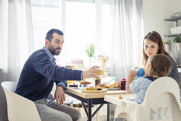 Man offering juice to son while having breakfast at table - CAVF44486