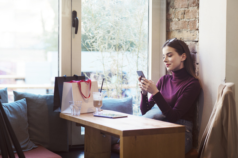 Frau, die ein Mobiltelefon benutzt, während sie in einem Cafe sitzt, lizenzfreies Stockfoto