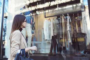 Side view of woman looking in shop window while shopping in city - CAVF44497