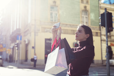 Woman with shopping bags photographing on city street during sunny day - CAVF44500