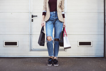 Low section of woman holding shopping bags while standing by closed door - CAVF44502