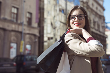 Glückliche Frau mit Einkaufstüten, die auf der Straße steht und wegschaut - CAVF44507