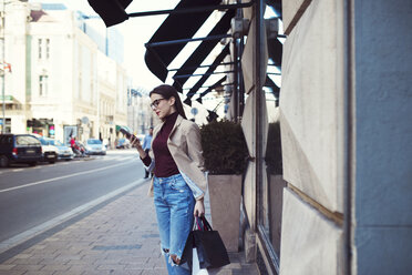 Frau mit Einkaufstüten, die ein Mobiltelefon benutzt, während sie auf dem Bürgersteig in der Stadt steht - CAVF44511