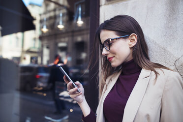 Frau benutzt Mobiltelefon, während sie an einer Mauer in der Stadt steht - CAVF44514