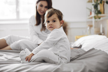 Porträt eines kleinen Jungen, der mit seiner Mutter zu Hause auf dem Bett sitzt - CAVF44519