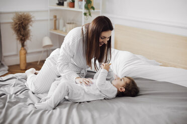 Happy mid adult woman looking at baby boy lying in bed at home - CAVF44520