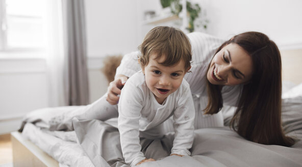 Porträt eines verspielten kleinen Jungen mit seiner Mutter auf dem Bett zu Hause - CAVF44522