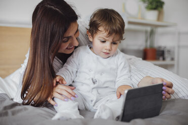 Glückliche Mutter, die einen Tablet-Computer mit einem kleinen Jungen im Bett benutzt - CAVF44527